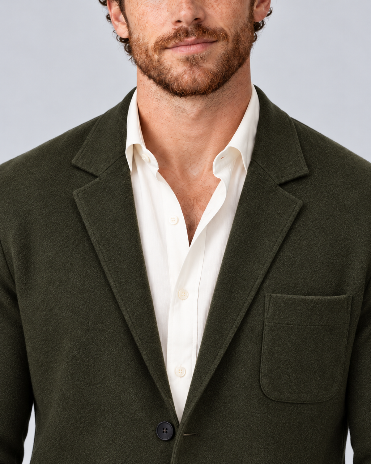 Men's knit blazer jacket in dark green, lapel and breast-pocket detail, photographed in a grey studio