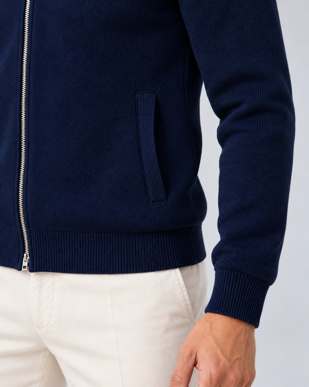 Men's full-zip collared knit jumper in navy blue, pocket knit and hem detail, photographed in a grey studio