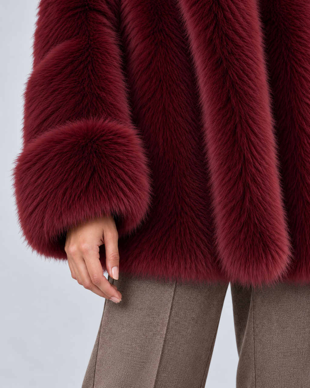 Women's short faux fur coat in burgundy, cuff and hem detail, photographed on a model in a grey studio