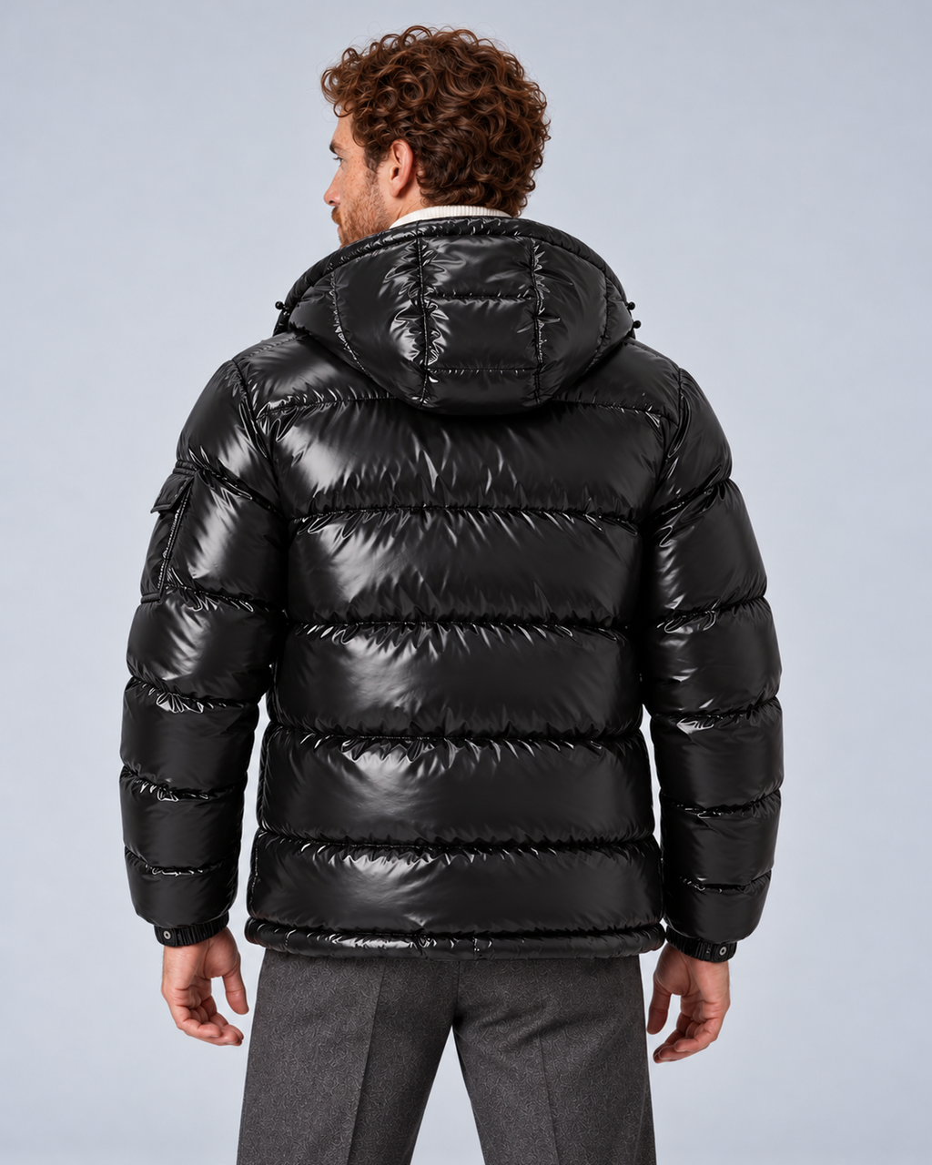 Men's glossy black puffer jacket with removable hood, rear with hood down, on a light grey studio background