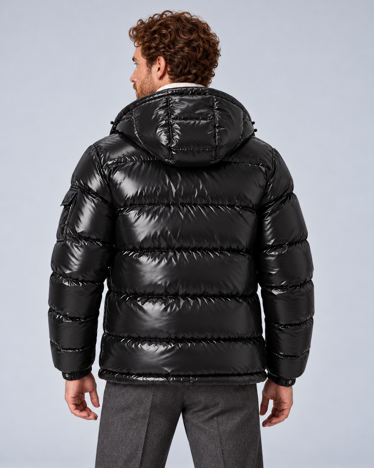 Men's glossy black puffer jacket with removable hood, rear with hood down, on a light grey studio background
