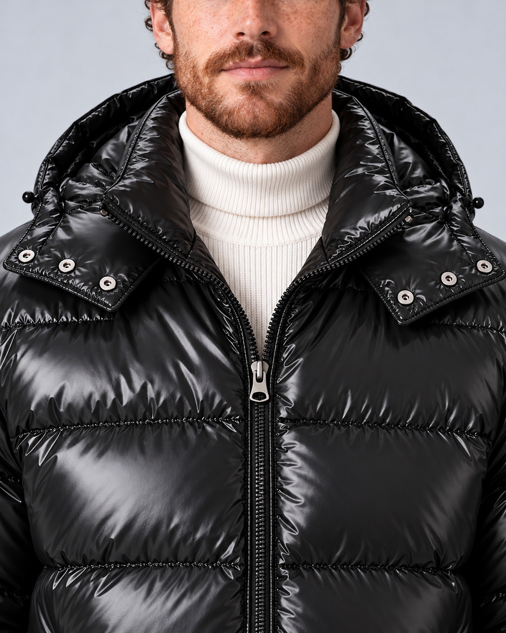 Men's glossy black puffer jacket with removable hood, collar and zipper detail, on a light grey studio background
