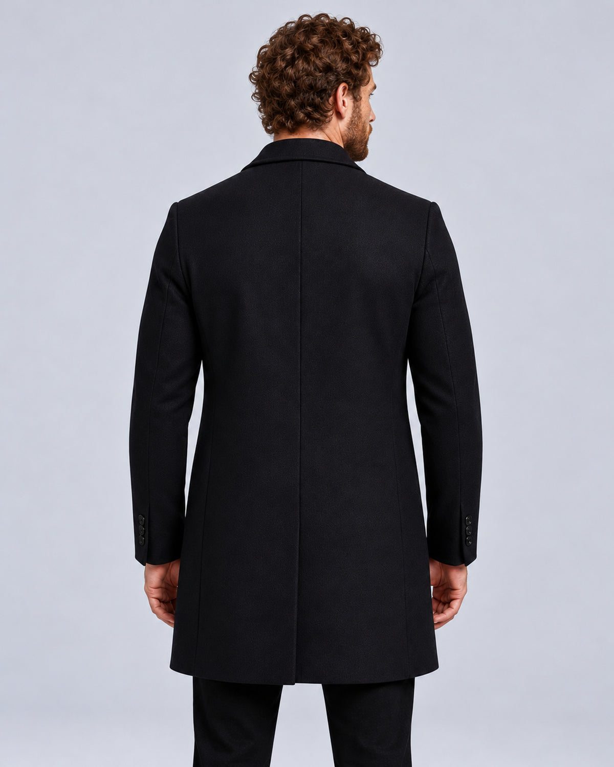 Men’s black tailored overcoat with notch lapels, rear view showing centre seam and button cuffs