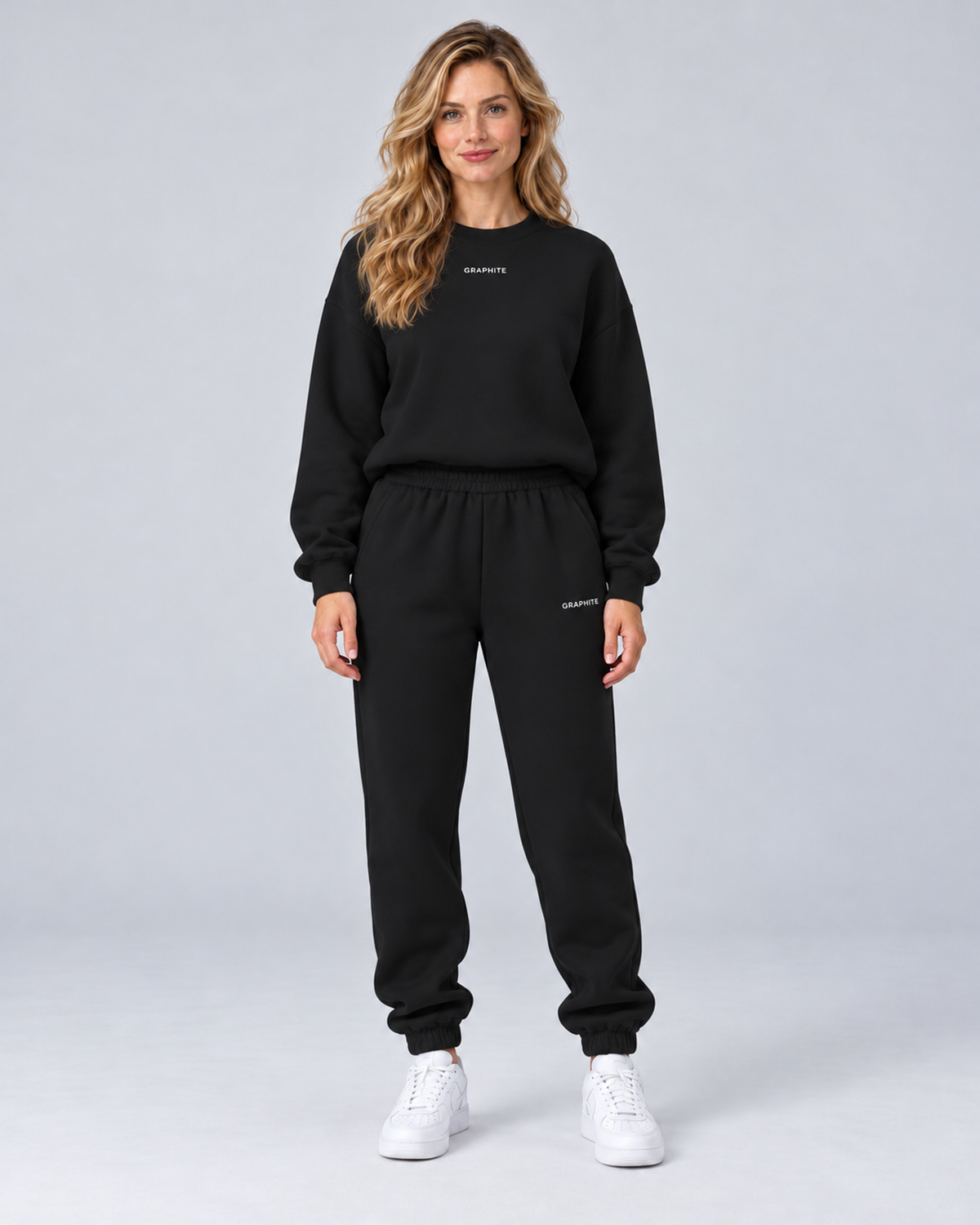 Front view of a black crewneck sweatshirt and cuffed joggers set with small embroidered lettering.