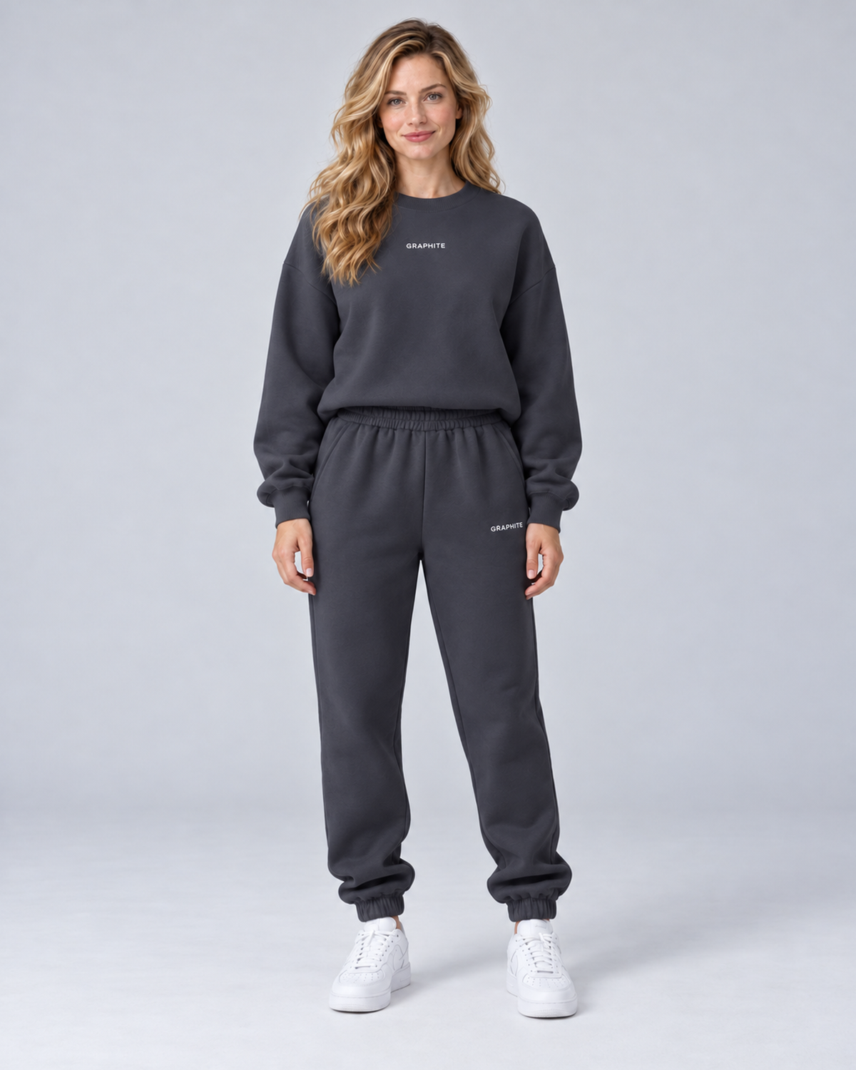 Front view of a dark grey crewneck sweatshirt and cuffed joggers set with small embroidered lettering.