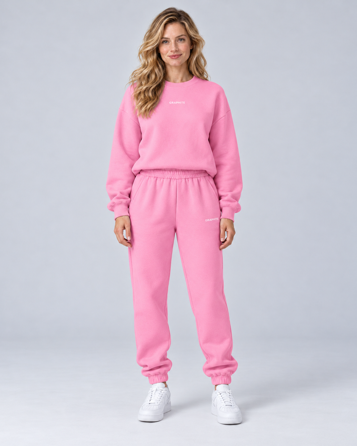 Front view of a pink crewneck sweatshirt and cuffed joggers set with small embroidered lettering.