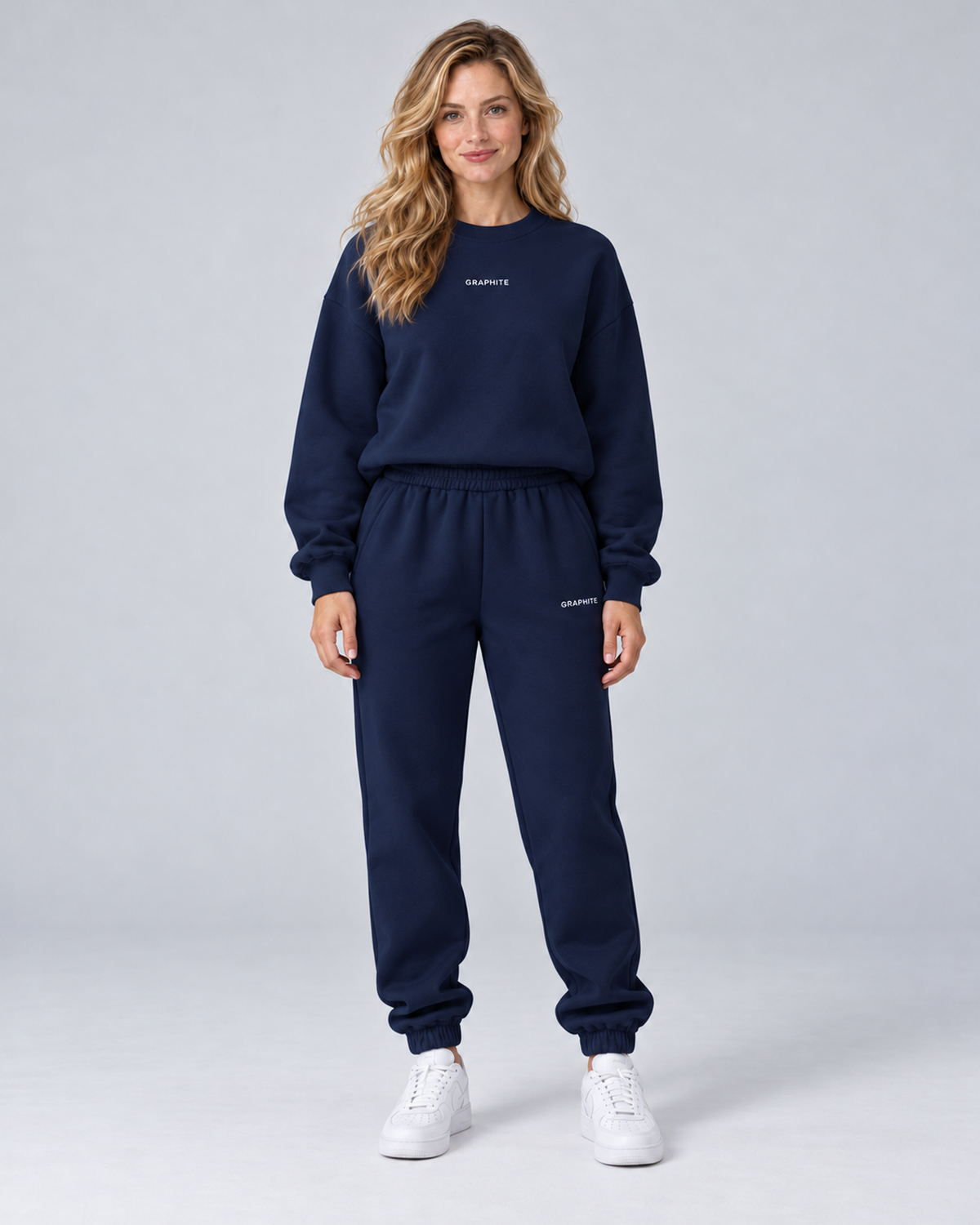 Front view of a navy blue crewneck sweatshirt and cuffed joggers set with small embroidered lettering.