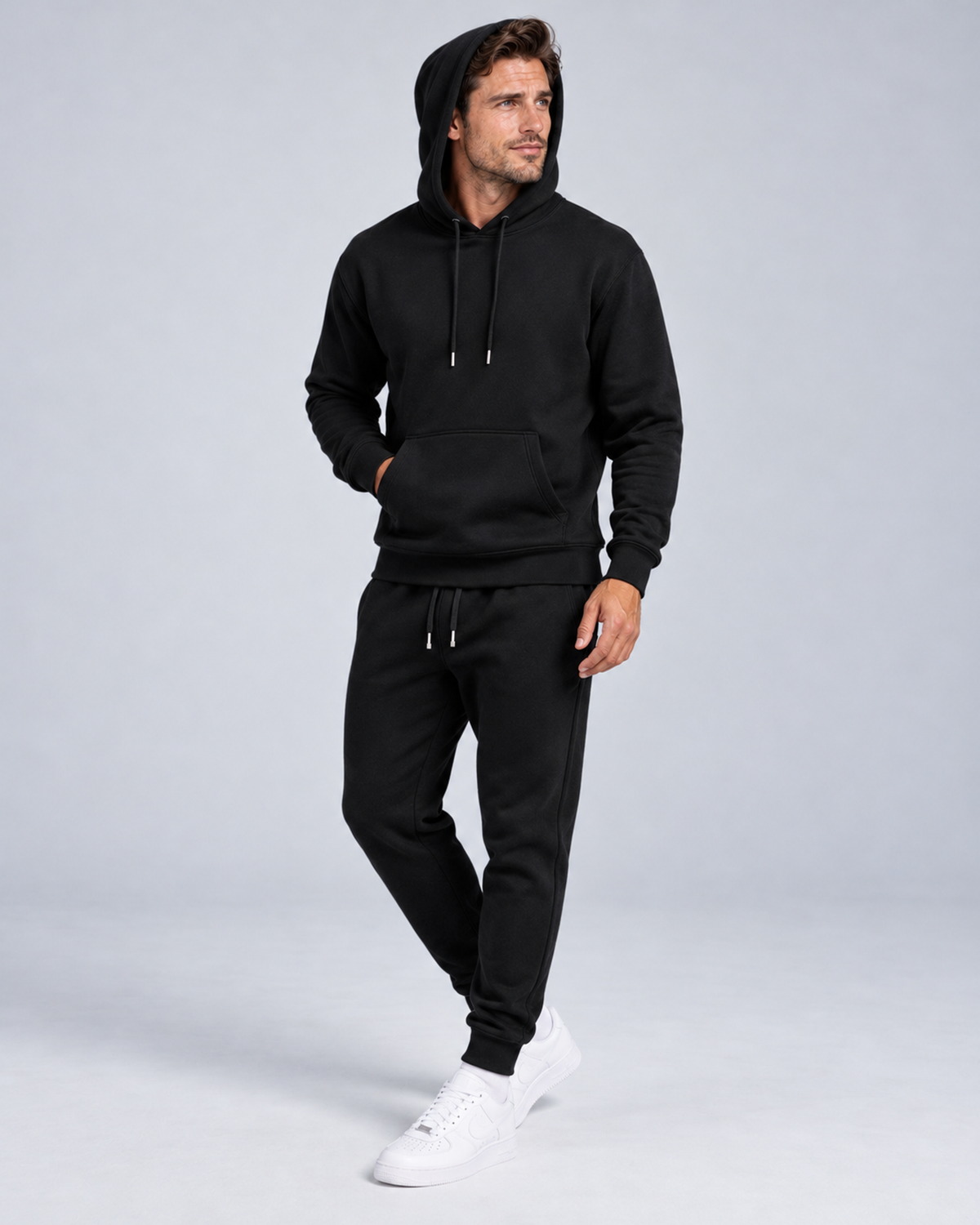 Men's pullover hoodie and cuffed jogger set in black, hood-up three-quarter, on approved studio model