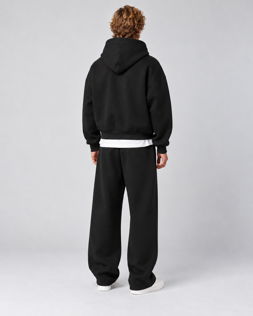 Men's black pullover hoodie and straight-leg tracksuit set, rear full-length view on approved studio model