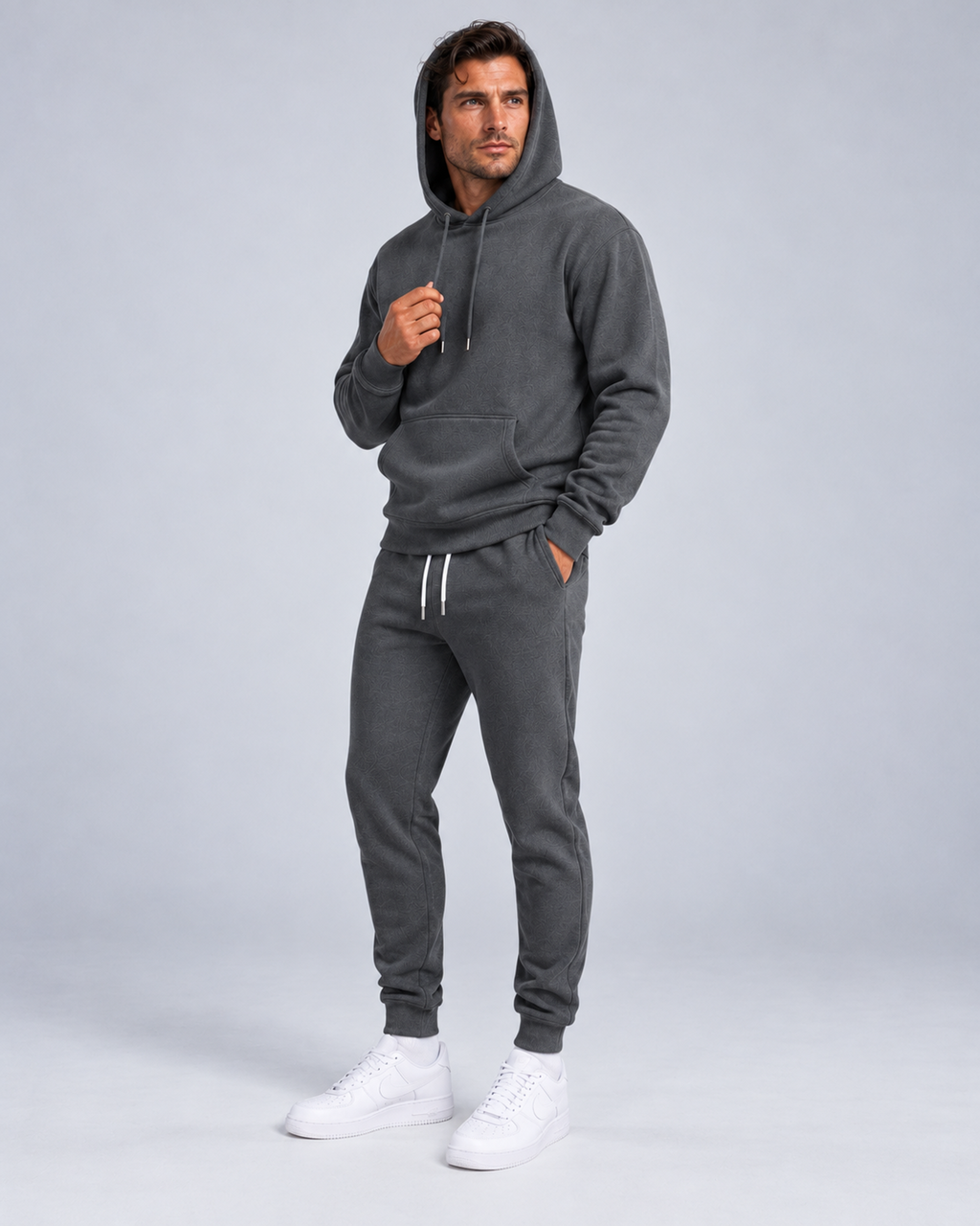 Men's pullover hoodie and cuffed jogger set in dark grey, hood-up three-quarter, on approved studio model