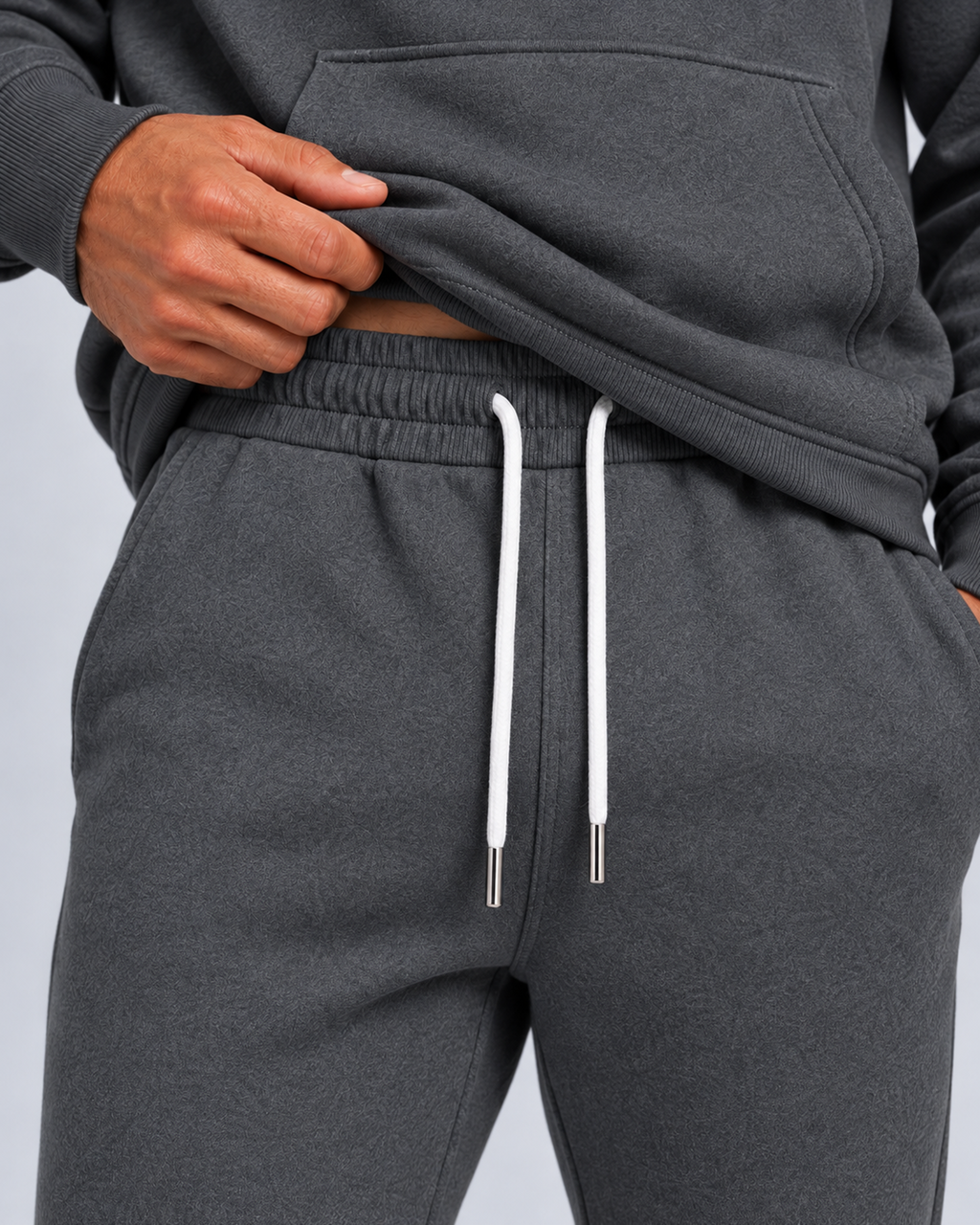 Men's pullover hoodie and cuffed jogger set in dark grey, waistband detail, on approved studio model